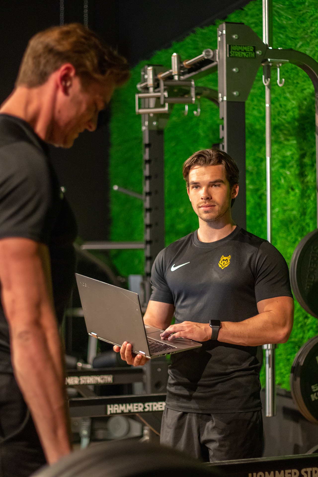 Coach bespreekt het trainingsplan met een lid op een laptop in de gym